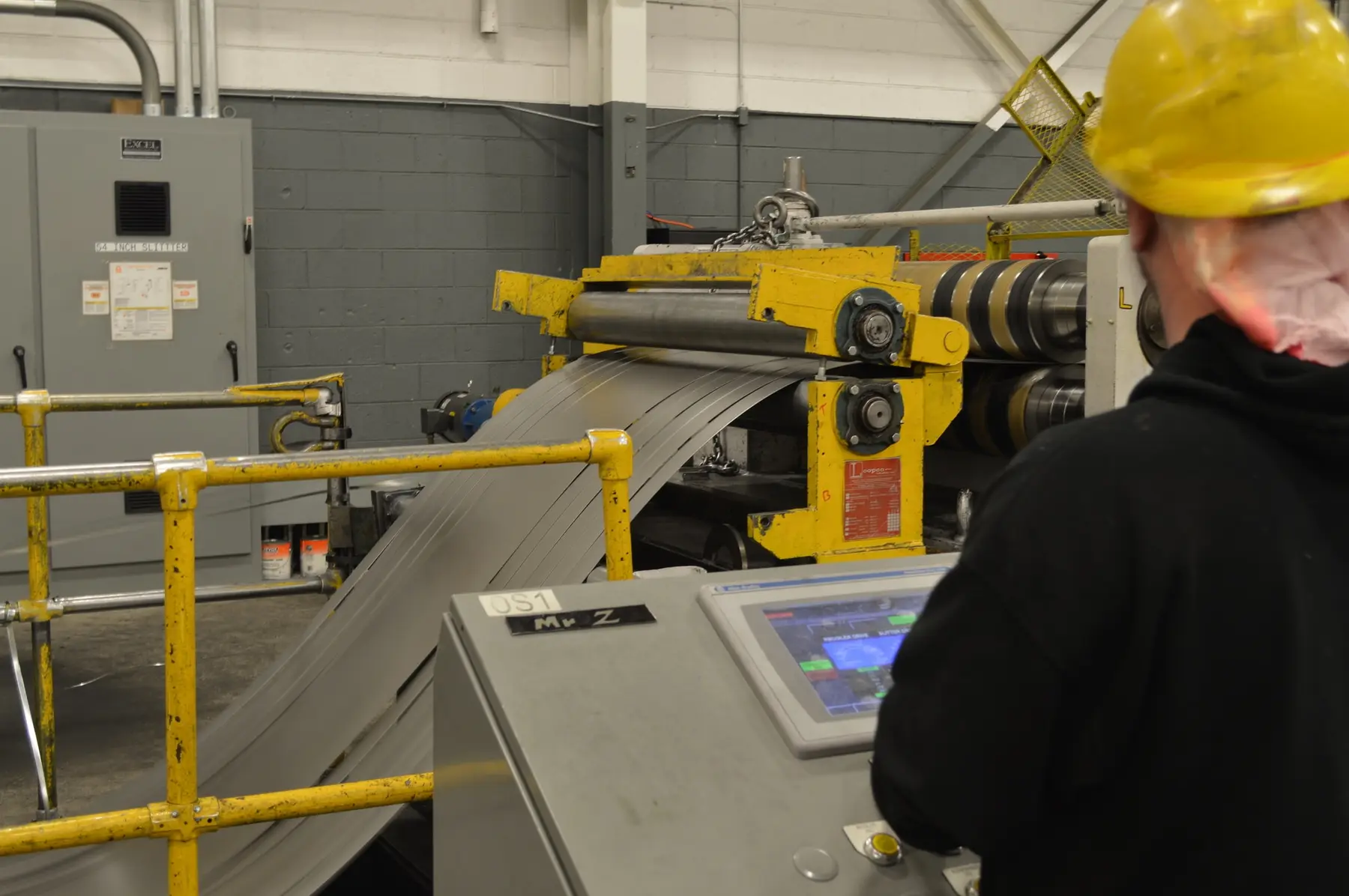 Steel strip running through an Alkar slitting line beside the operator control console