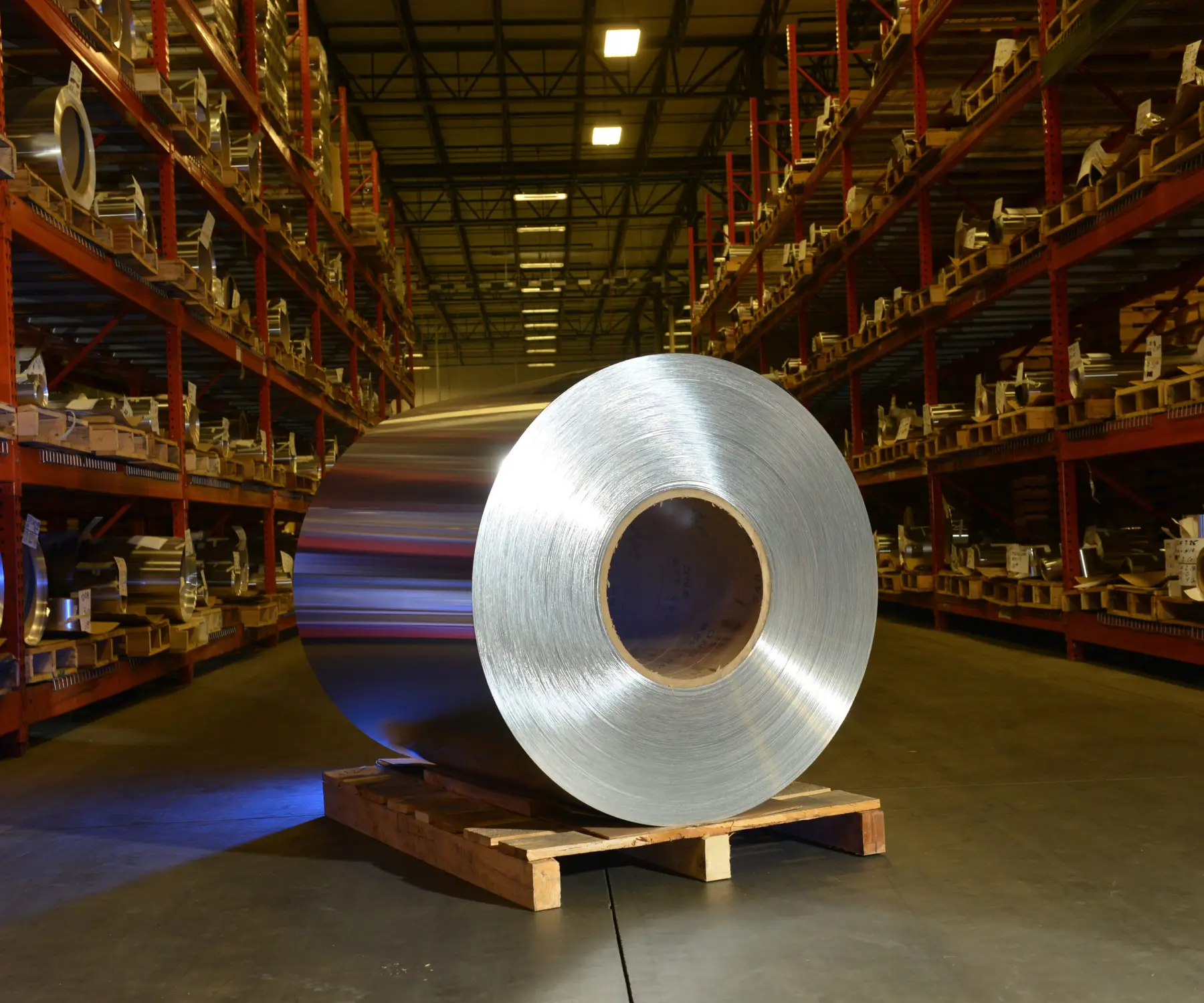 Aluminum foil coil on a skid in front of racked coil inventory in the All Foils warehouse