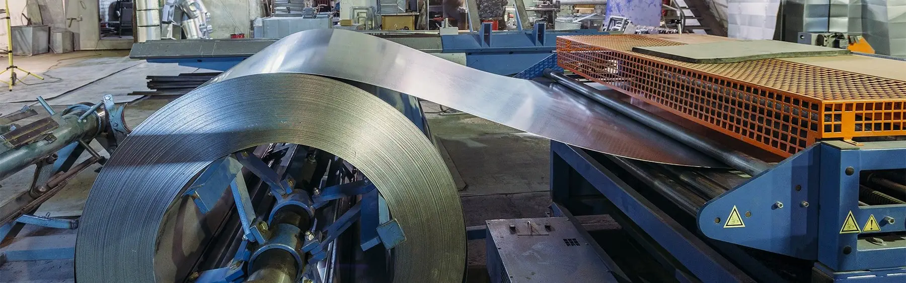 Steel coil unwinding into a processing line beside an orange safety guard