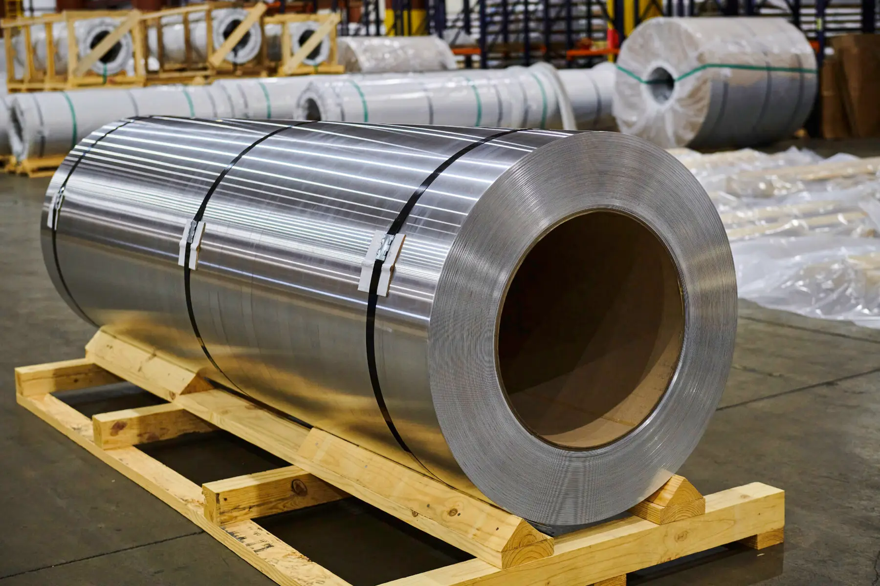 Banded aluminum coil on a wooden skid in front of rows of stocked coils in a Champagne Metals warehouse