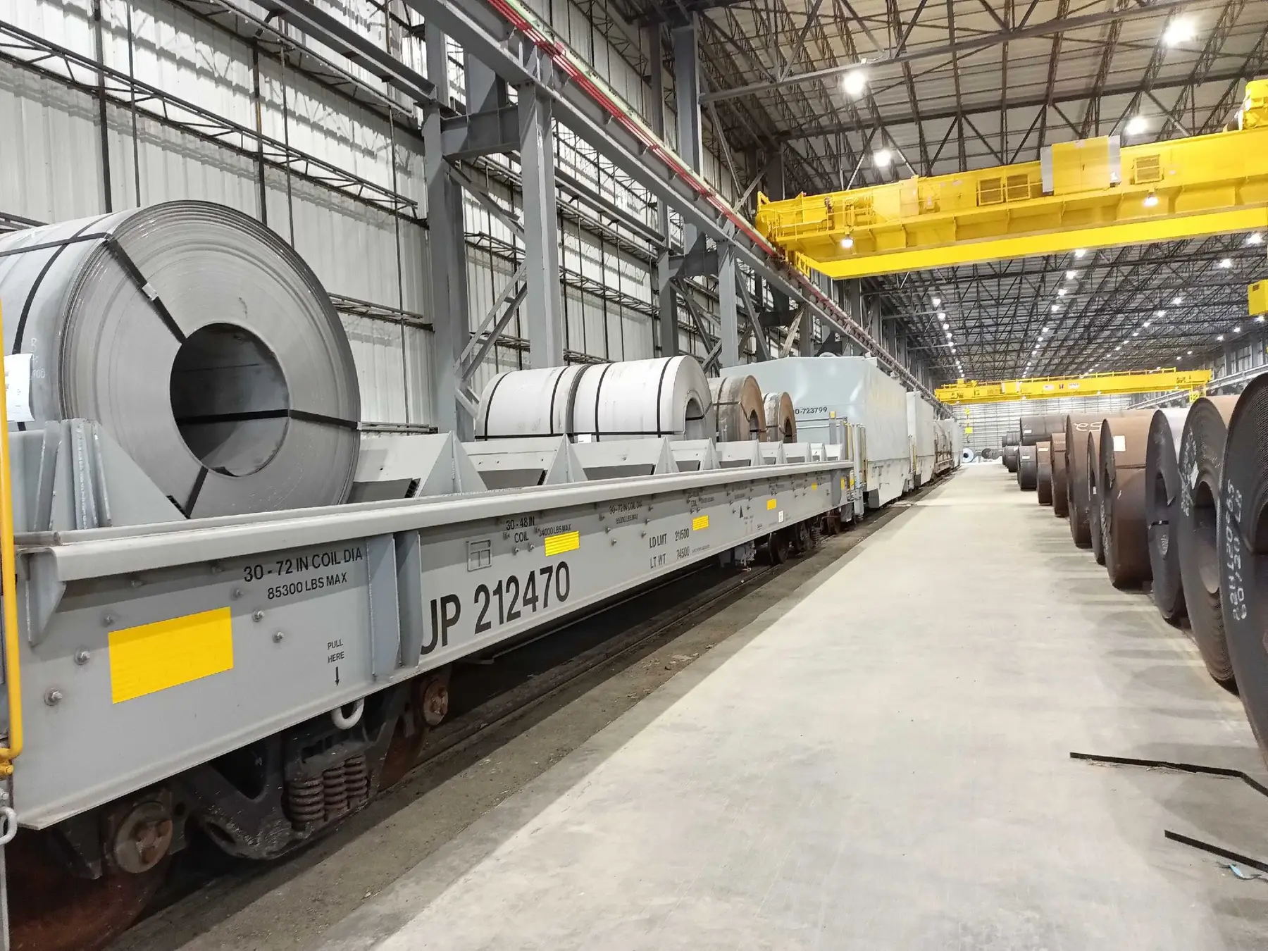 Hot-rolled master coils staged beside a rail car in the Ferrous 85 coil bay under overhead cranes