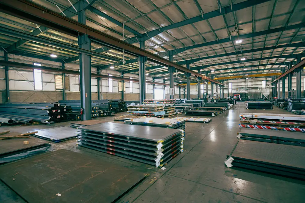 Stacks of cut steel plate on the floor of a Harbor Steel warehouse under overhead cranes