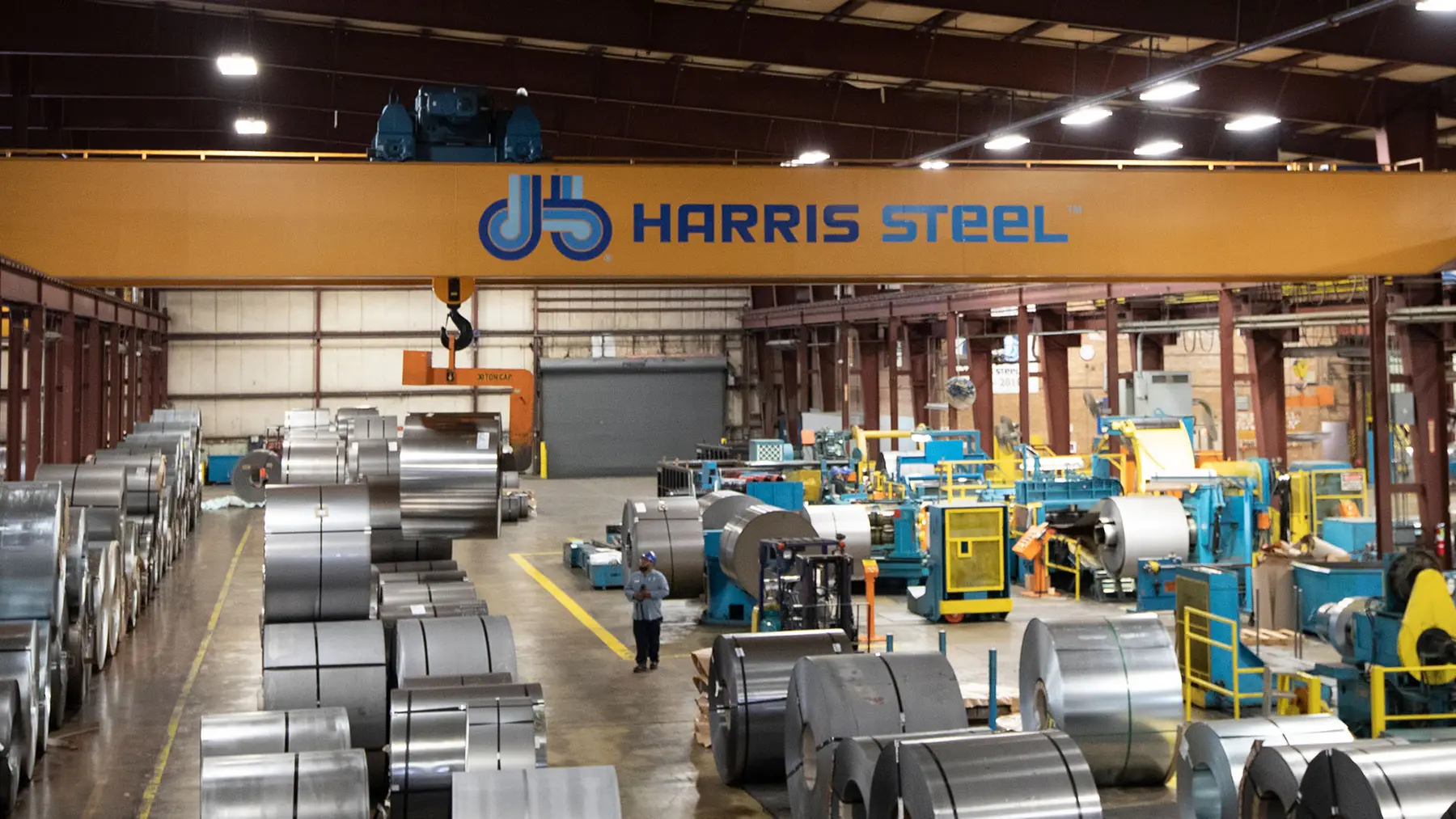 Harris Steel plant floor in Cicero with a slitting line, slit coils and an overhead crane bearing the company logo