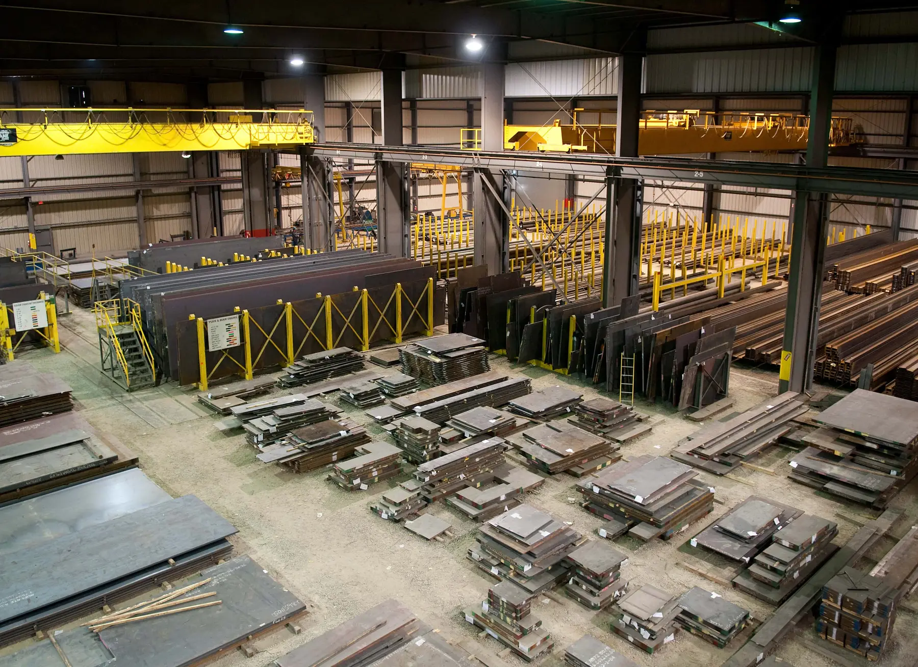 Overhead view of an Infra-Metals warehouse bay with stacked steel plate and overhead cranes