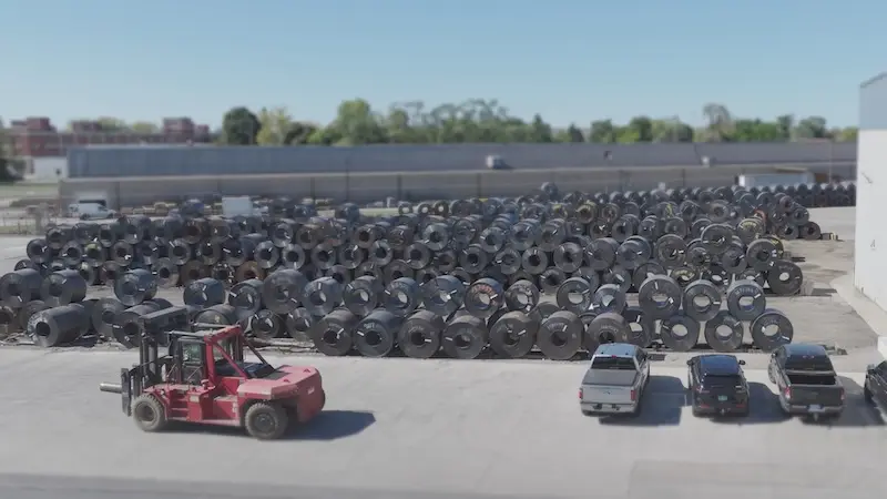 Outdoor storage yard holding rows of Kenwal Steel coil inventory with a forklift