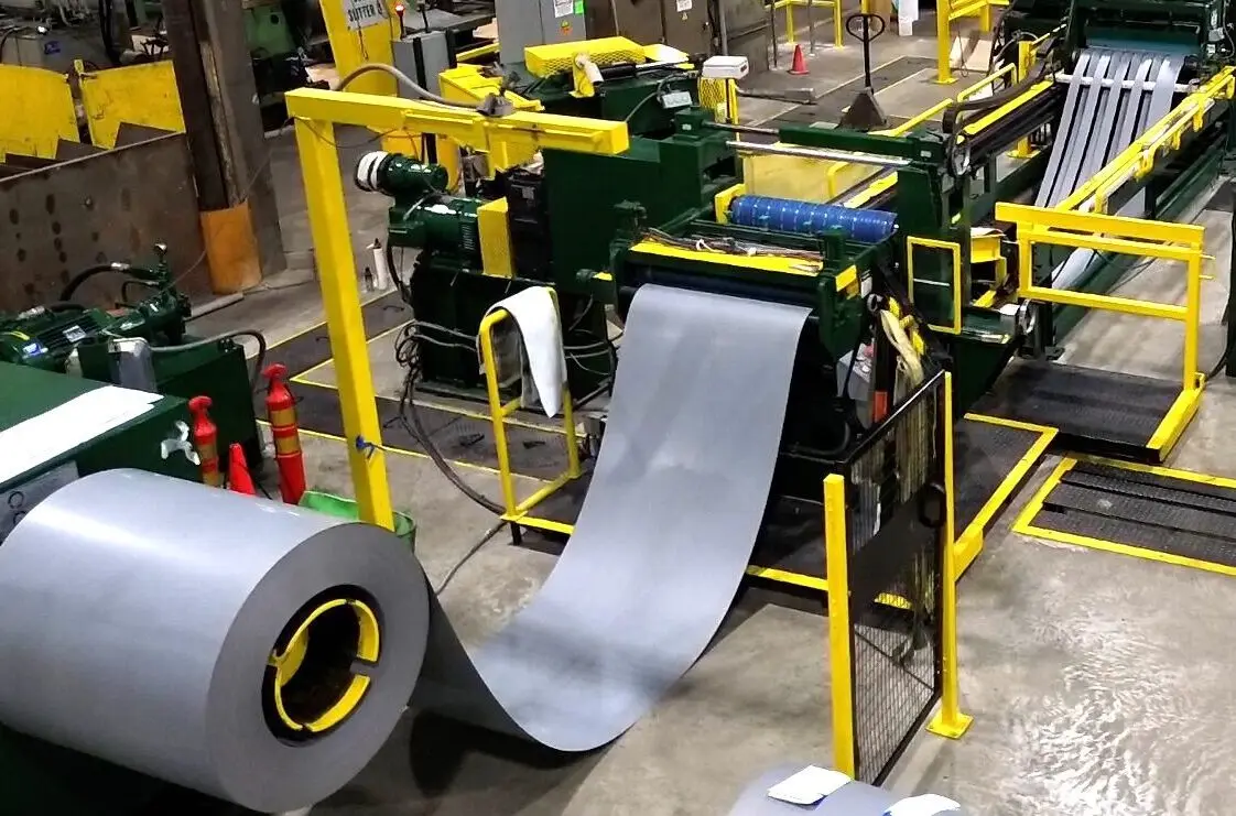 Steel coil unwinding into a slitting line with yellow safety guarding
