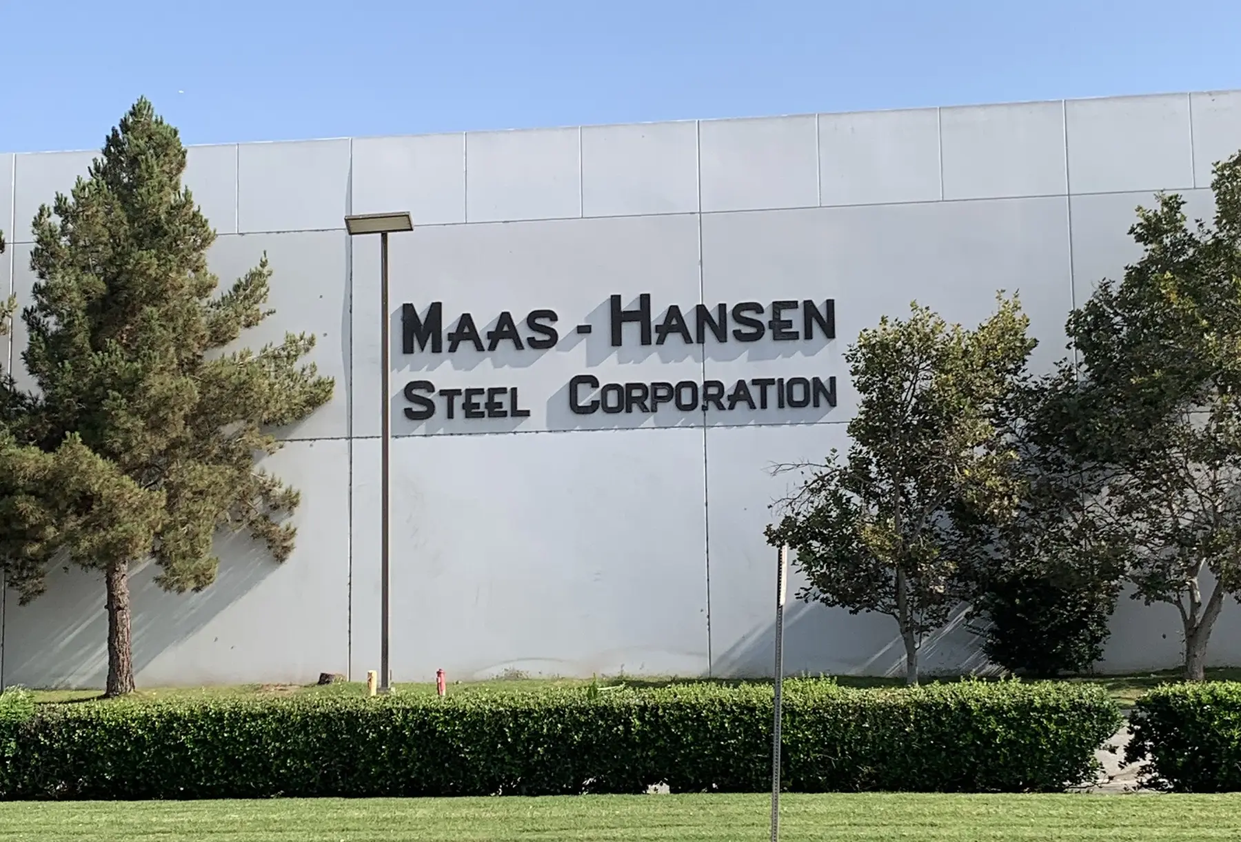 Maas-Hansen Steel Corporation building sign behind trees and landscaping
