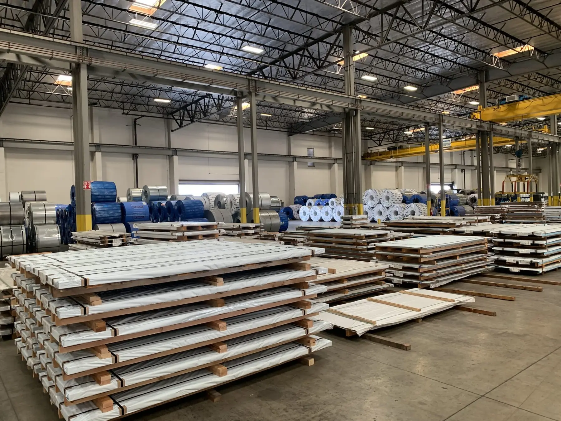 Stacks of leveled steel sheets and wrapped coils across the Maas-Hansen Steel plant floor