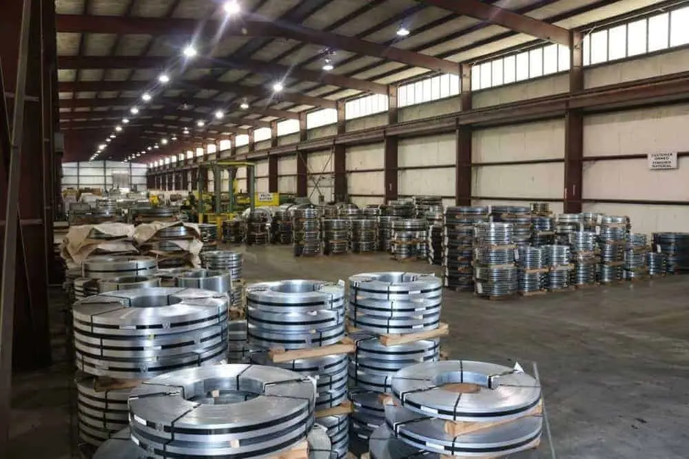 Warehouse floor lined with rows of banded slit steel coils under high bay lighting