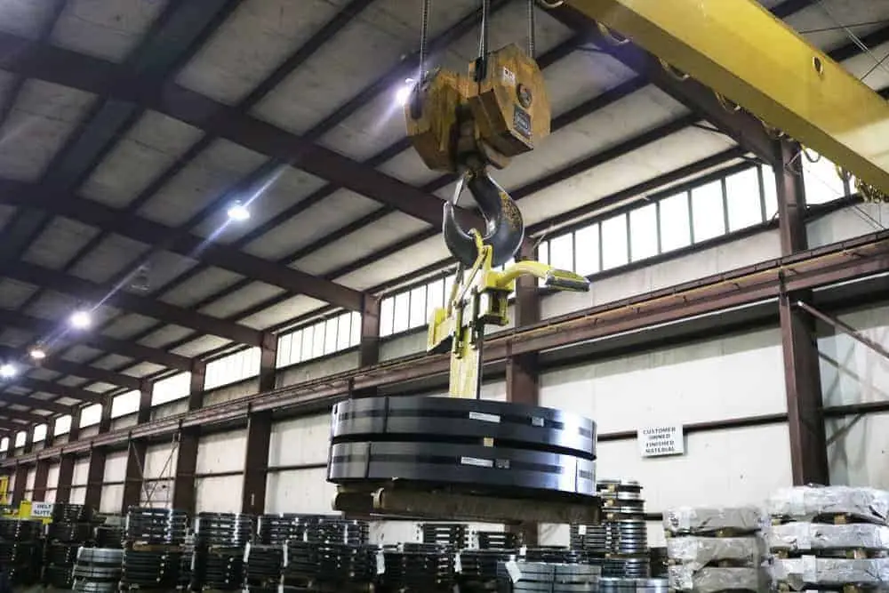 Overhead crane lifting a stack of slit steel coils above the plant floor