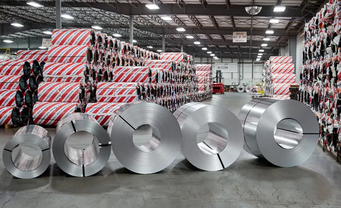 Bare steel coils in front of stacks of red-and-white wrapped coils in warehouse