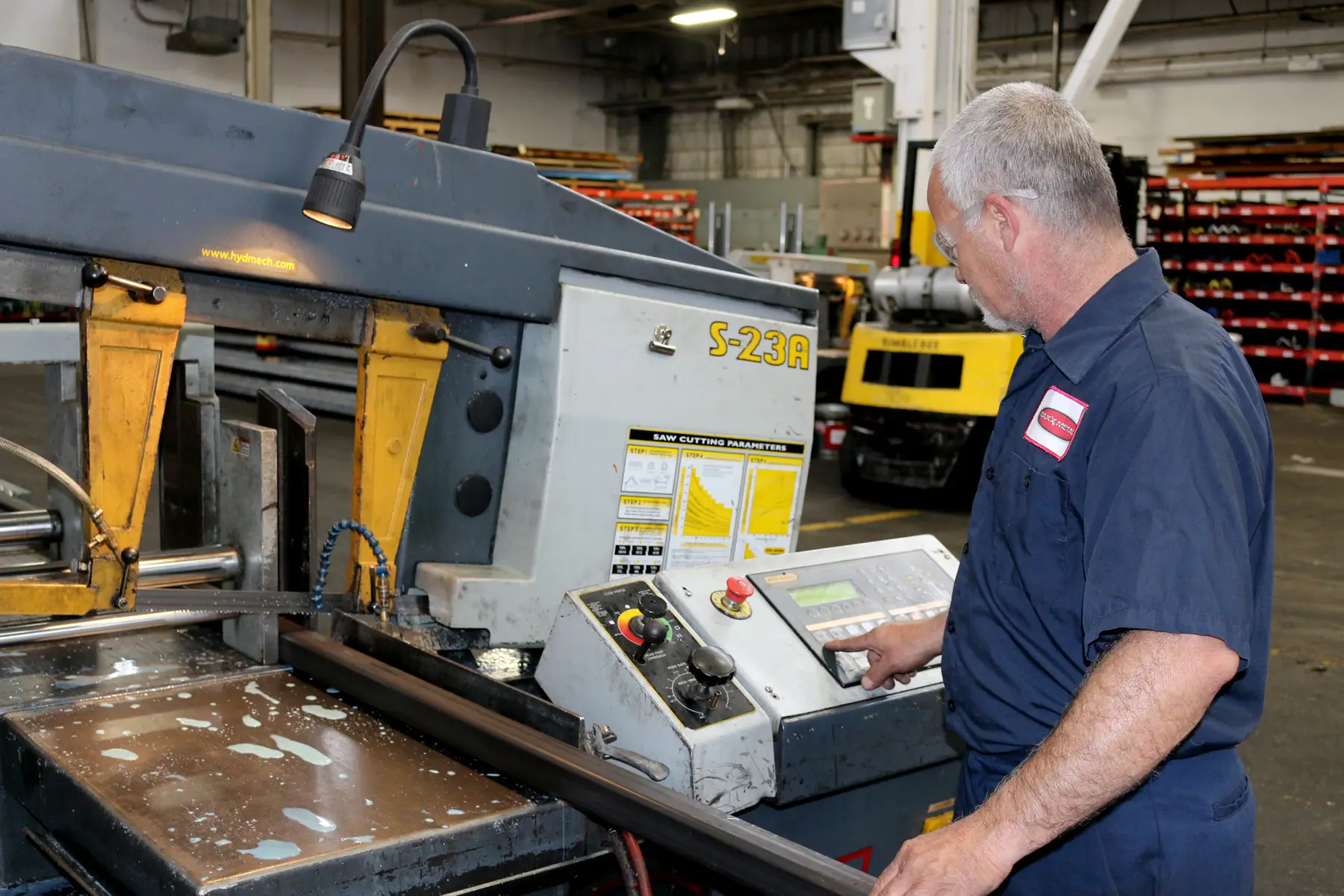 Operator running a programmable band saw beside stock racks in the Maxx Metals warehouse