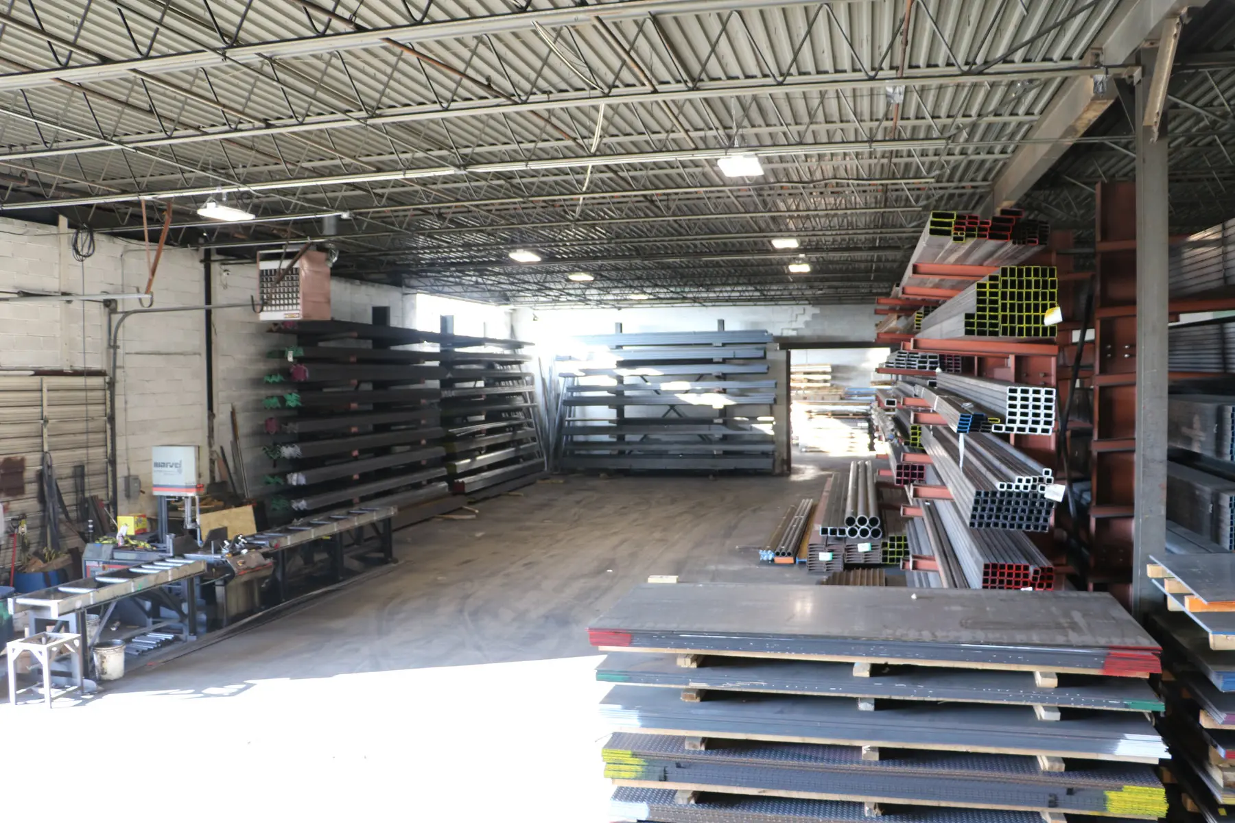 Inside the Metal Masters warehouse with stacked plate, cantilever racks of bar and tube, and a saw station