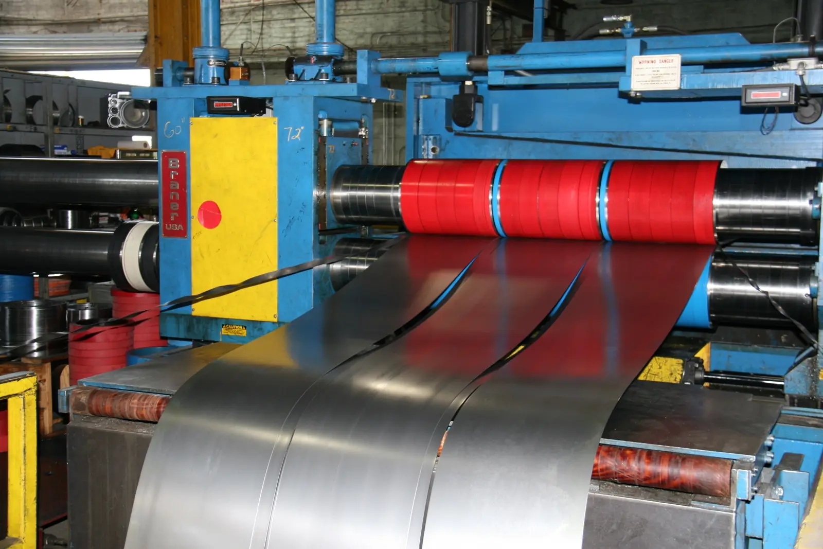 Steel strip passing through a slitter head with red separator rolls on Midland Steel's slitting line
