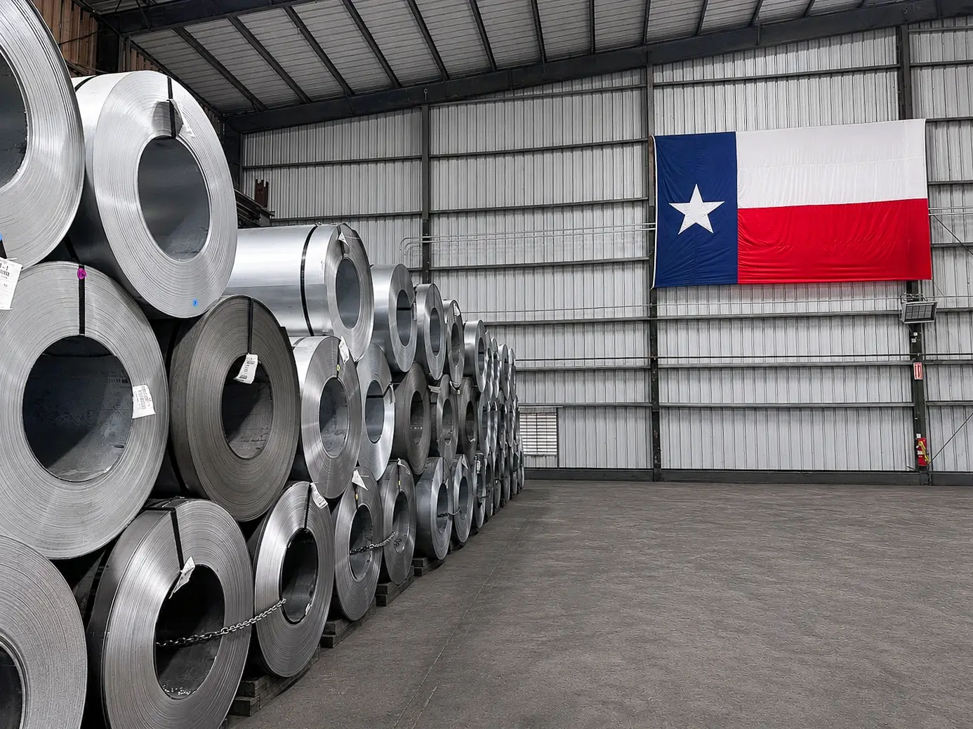 Steel coils stacked inside Mill Steel's Houston facility beneath a Texas flag