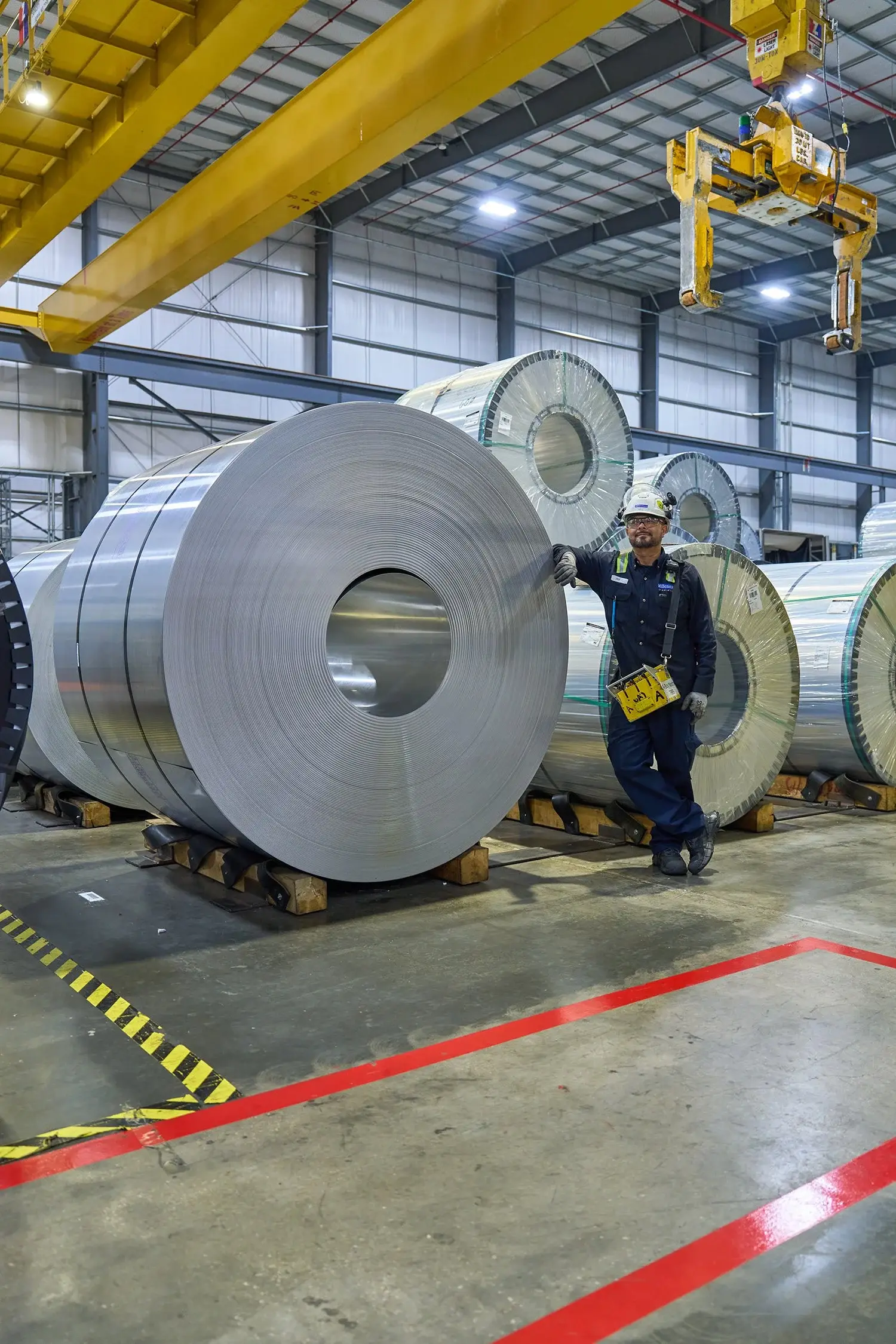 Large steel master coils on the floor of Millennium Steel's warehouse bay beneath overhead cranes