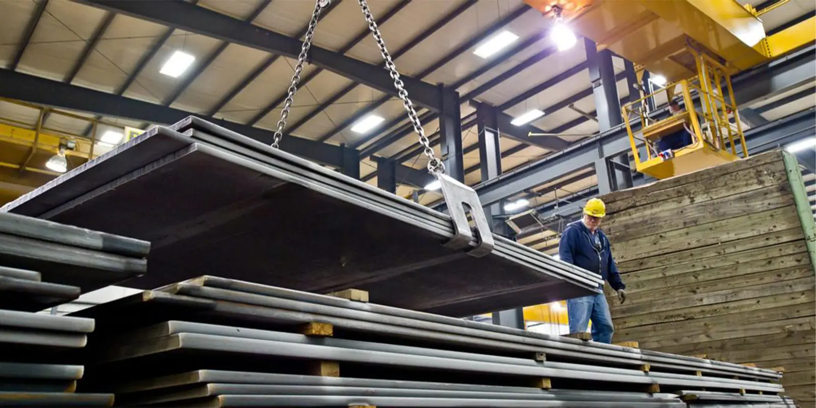 Overhead crane lifting steel plate above stacked inventory in a Norfolk Iron & Metal warehouse