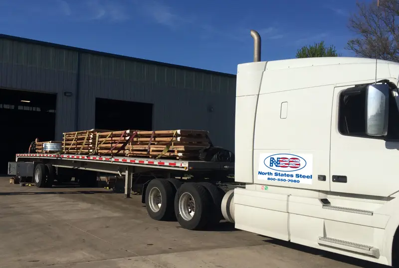 North States Steel truck with crated steel sheets and a coil loaded on its flatbed at the warehouse dock
