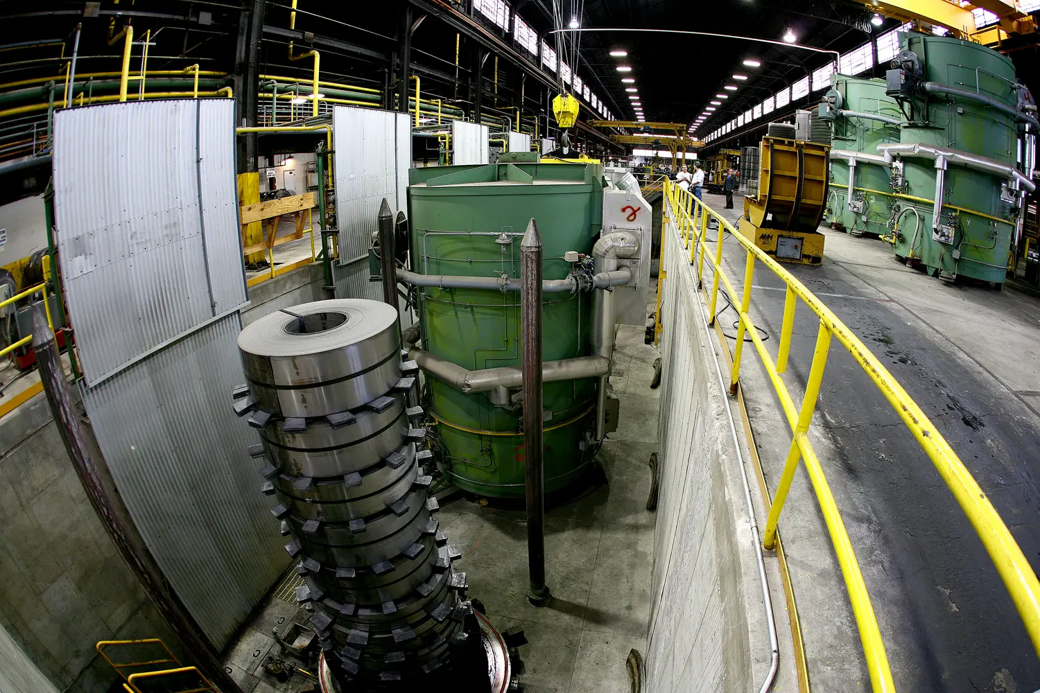 Stacked strip coils beside annealing bases along a walkway in the plant