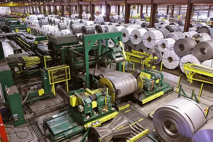 Coil processing line uncoiling steel beside rows of stored coils at Olympic Steel's Minneapolis coil facility