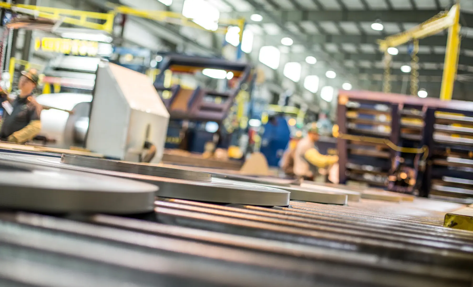 Slit metal strip running through a slitting line with operators in the background