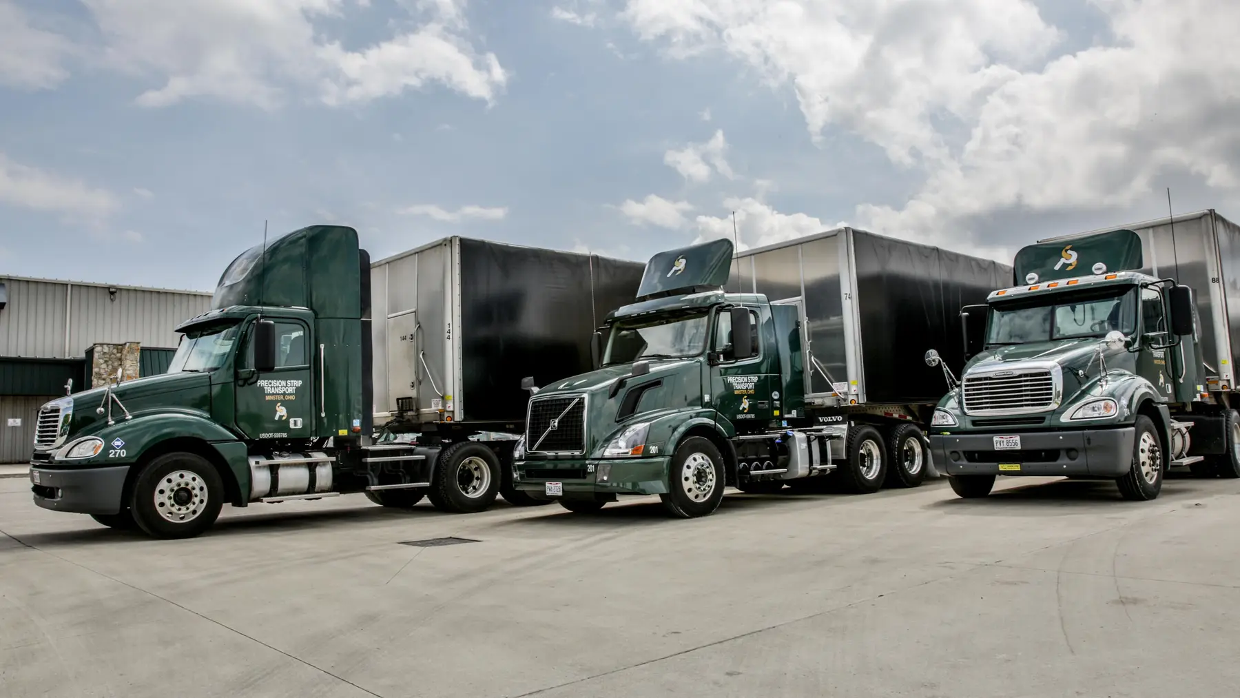 Three green Precision Strip tractor-trailers parked outside a processing plant