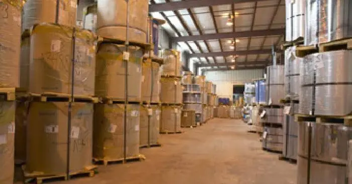 Warehouse aisle lined with paper-wrapped and bare stainless and aluminum coils on pallets