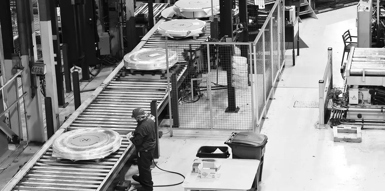 Packaged Randall Metals slit coils moving along a roller conveyor at the end of a slitting line
