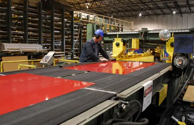 Red-coated steel sheet running out of a Ryerson cut-to-length line beside racked sheet inventory