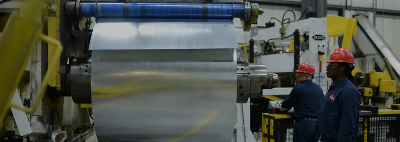 Flat-rolled steel coil mounted on a processing line with operators at the controls