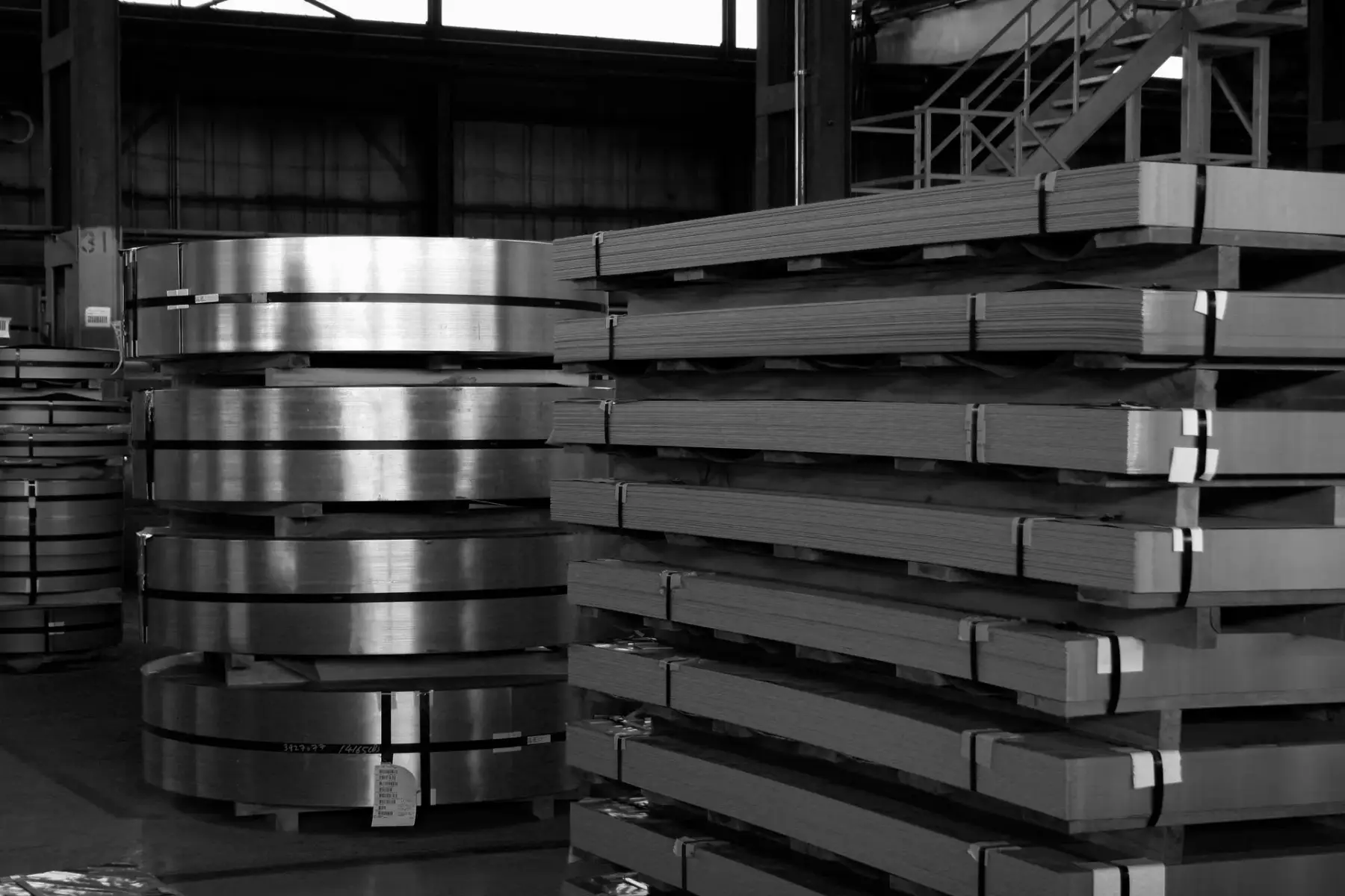 Stacked flat-rolled steel coils and banded sheet bundles in warehouse storage