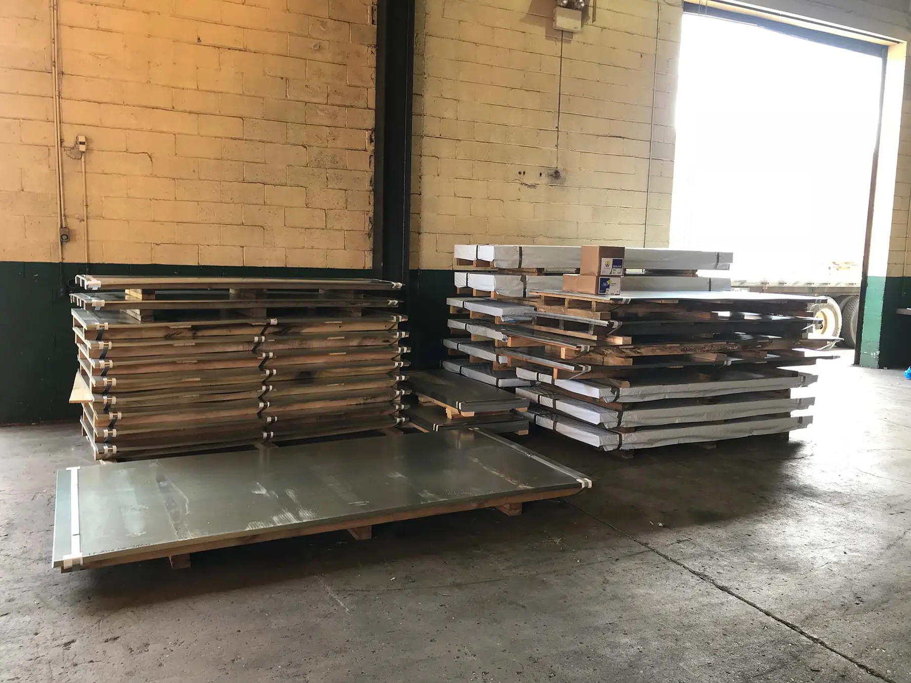Stacks of cut metal sheets staged by a loading door at Sherwood Steel