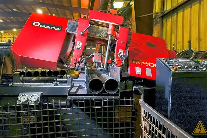 Red Amada automatic band saw cutting a bundle of steel pipe at State Line Supply