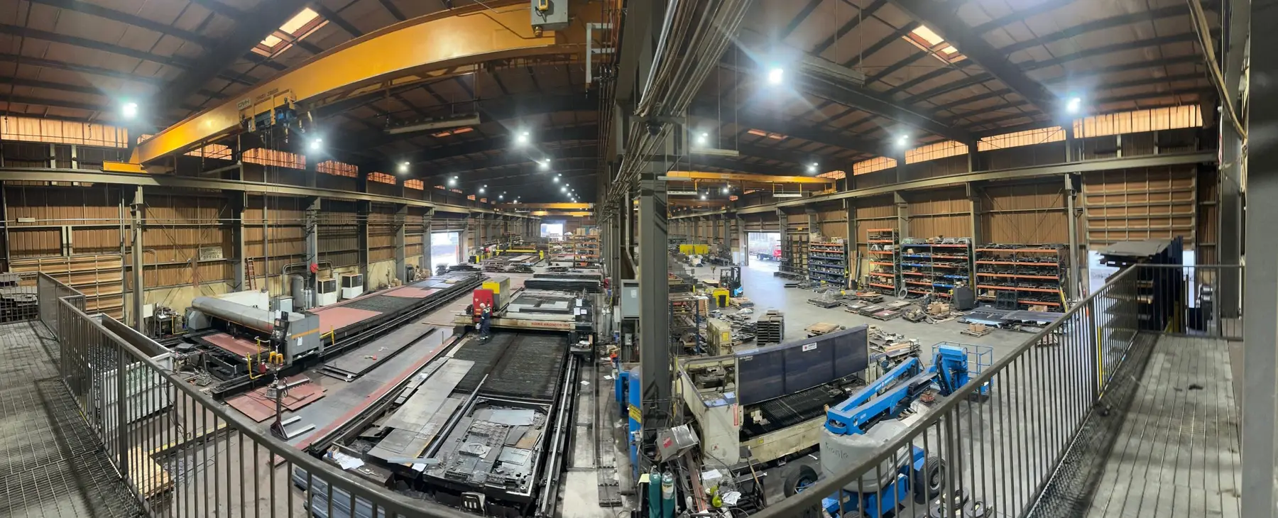 Wide view of the Tacoma Steel plant floor with overhead cranes, cutting tables and steel stock