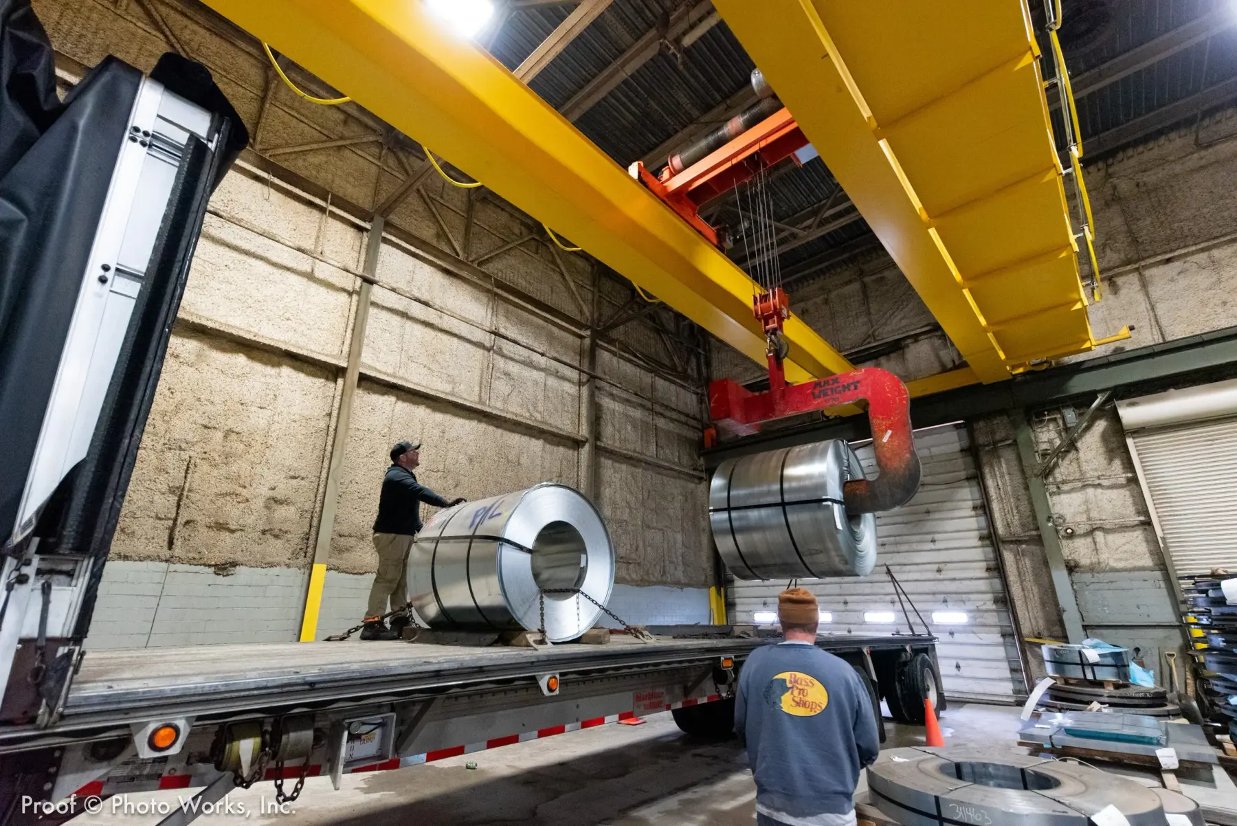 Overhead crane lowering a steel coil onto a flatbed trailer inside the Universal Metals warehouse