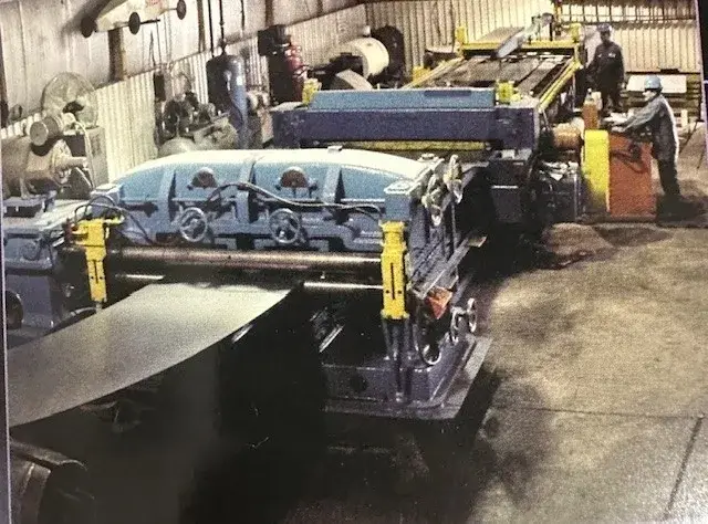 Steel sheet running through a slitter with operators working at the line