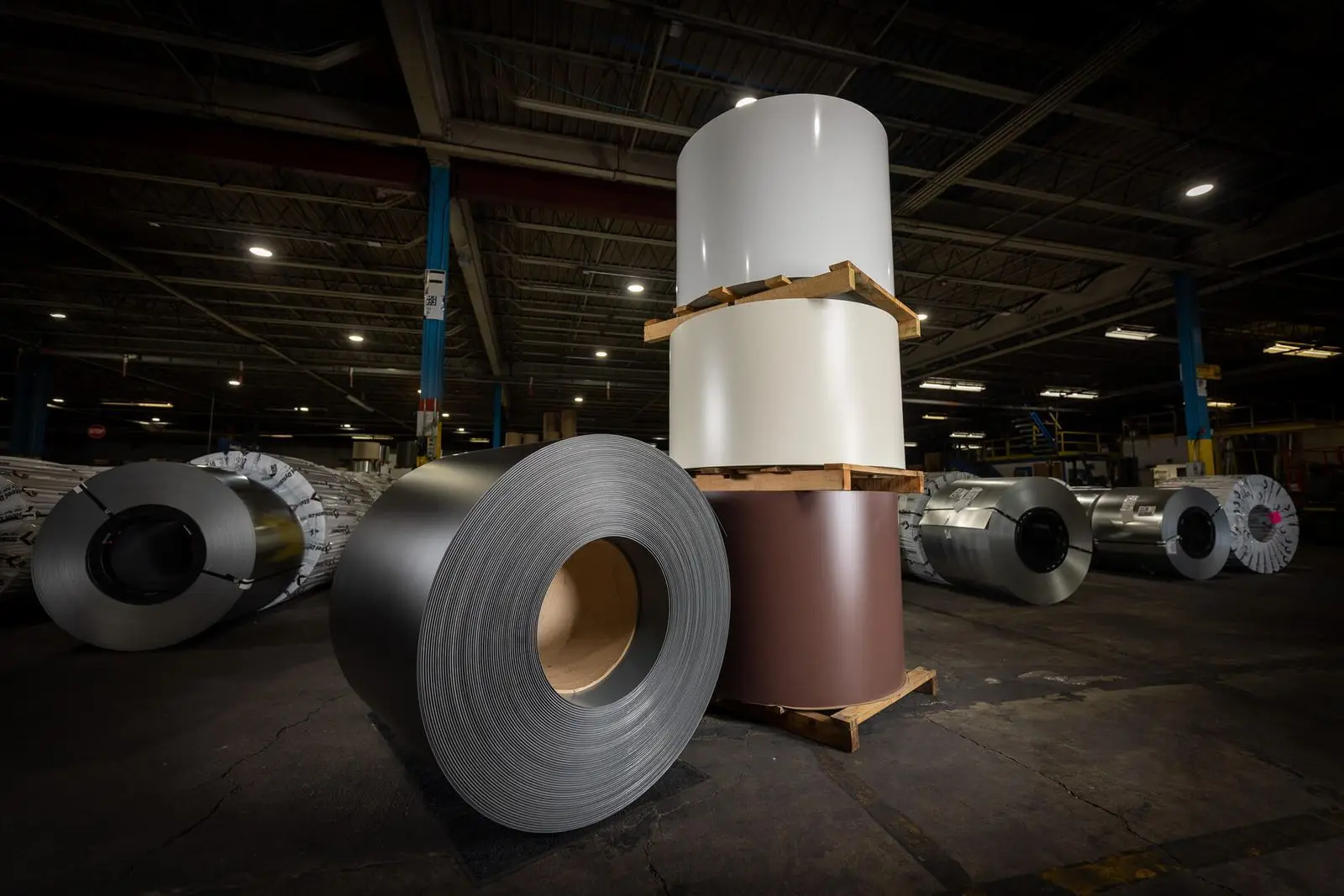 Coated steel coils, including white and brown painted coils, staged on the floor of a VORTEQ coil coating plant