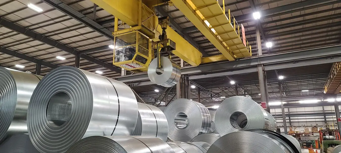 Overhead crane lifting a steel coil above rows of galvanized coils inside a Worthington Steel plant